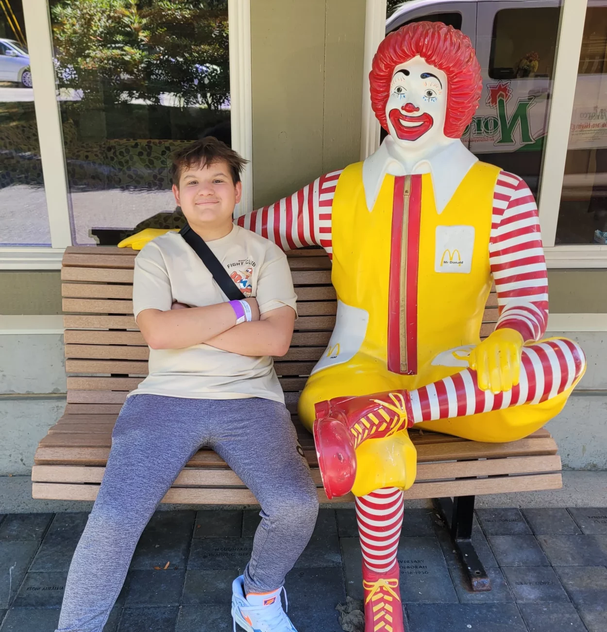 Teenage boy Kyler sitting outside on a bench next to statue of Ronald McDonald